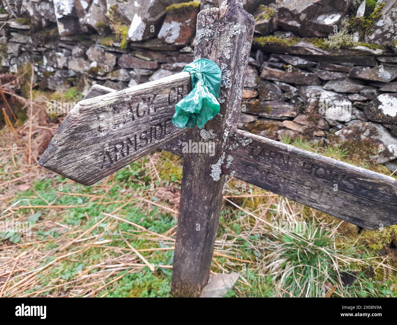 A rather delightfully placed dog poo bag on a signpost near Tarn Hows in the Lake District Stock Photo