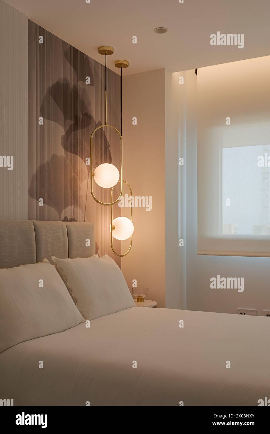 A modern bedroom featuring a plush bed with white bedding and stylish wall-mounted lights with spherical shades, casting a warm glow Stock Photo