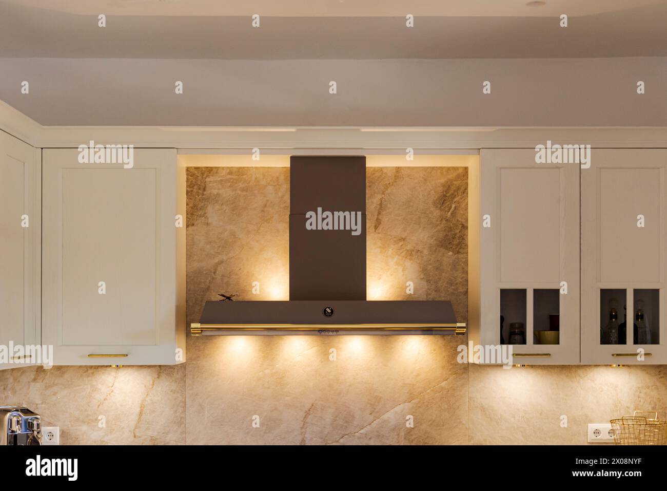 Elegant modern kitchen featuring a sleek range hood, warm under lighting, and white