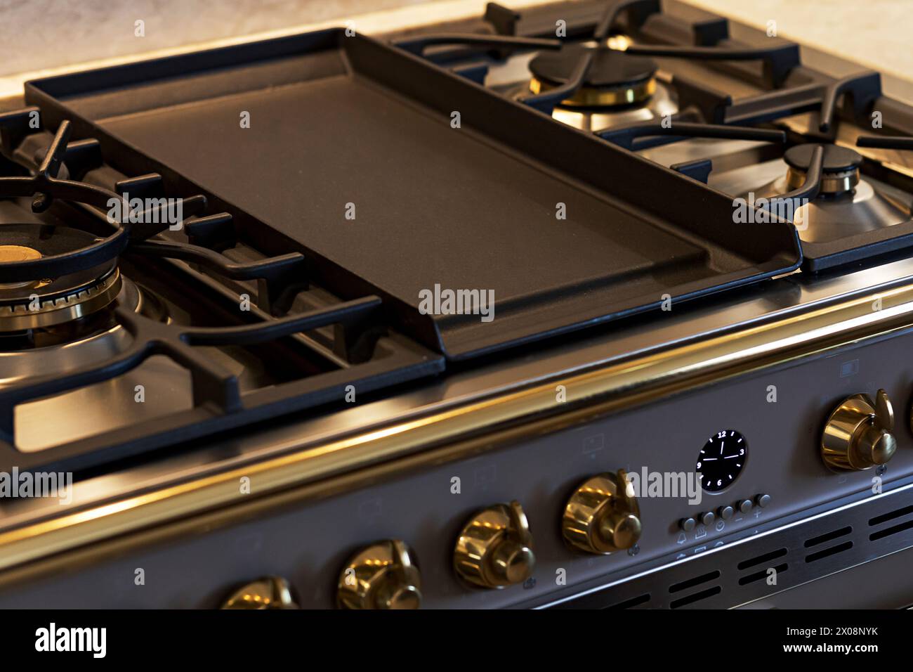 Modern gas stove with a large cast-iron griddle and stylish brass knobs in a luxury kitchen setup Stock Photo