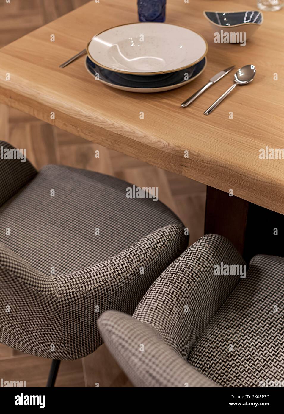 A stylish table setting featuring a wooden dining table with elegant dinnerware and comfortable patterned chairs in a warm, inviting atmosphere Stock Photo