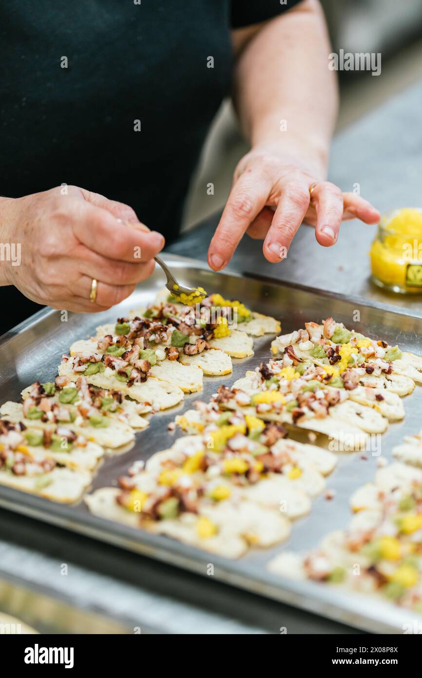 Anonymous hands garnish freshly baked savory biscuits with colorful toppings, preparing for an exquisite culinary presentation Stock Photo