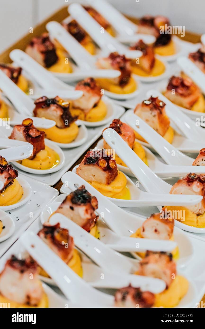 Rows of chic white spoons hold perfectly cooked octopus pieces atop a dollop of sauce, ready for a high-end gastronomic event Stock Photo
