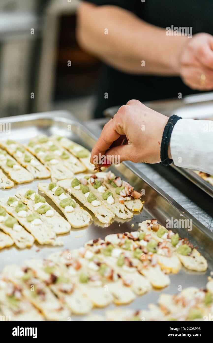 Anonymous chef meticulously adds final toppings to an array of canapes on a stainless steel tray, showcasing the precision of culinary art Stock Photo