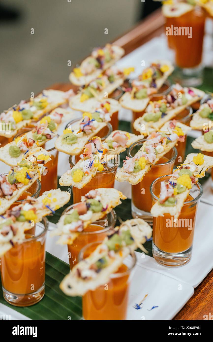 A sophisticated culinary setup featuring shot glasses of gazpacho soup garnished with exquisitely prepared gourmet toppings Stock Photo