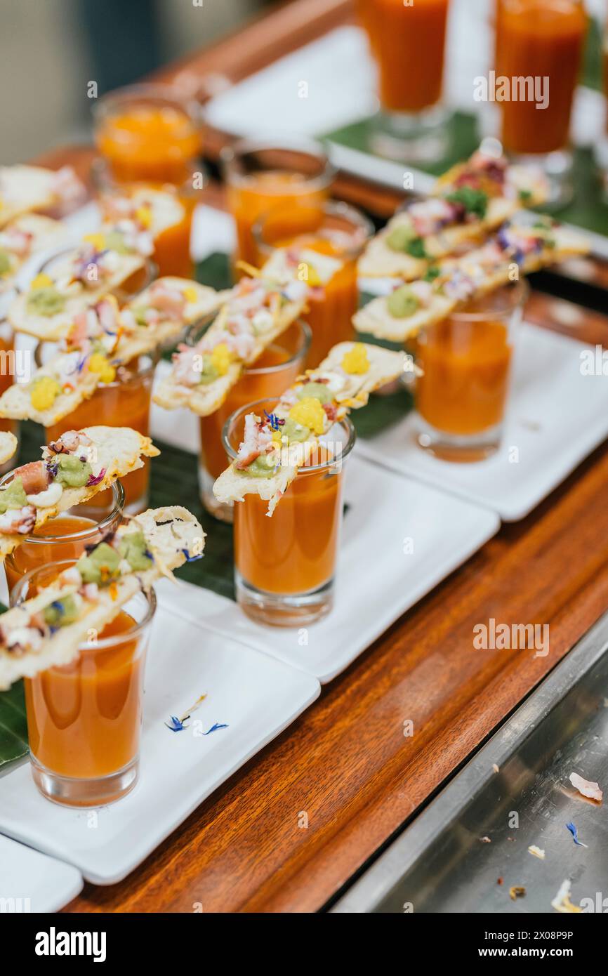 A sophisticated culinary setup featuring shot glasses of gazpacho soup garnished with exquisitely prepared gourmet toppings Stock Photo