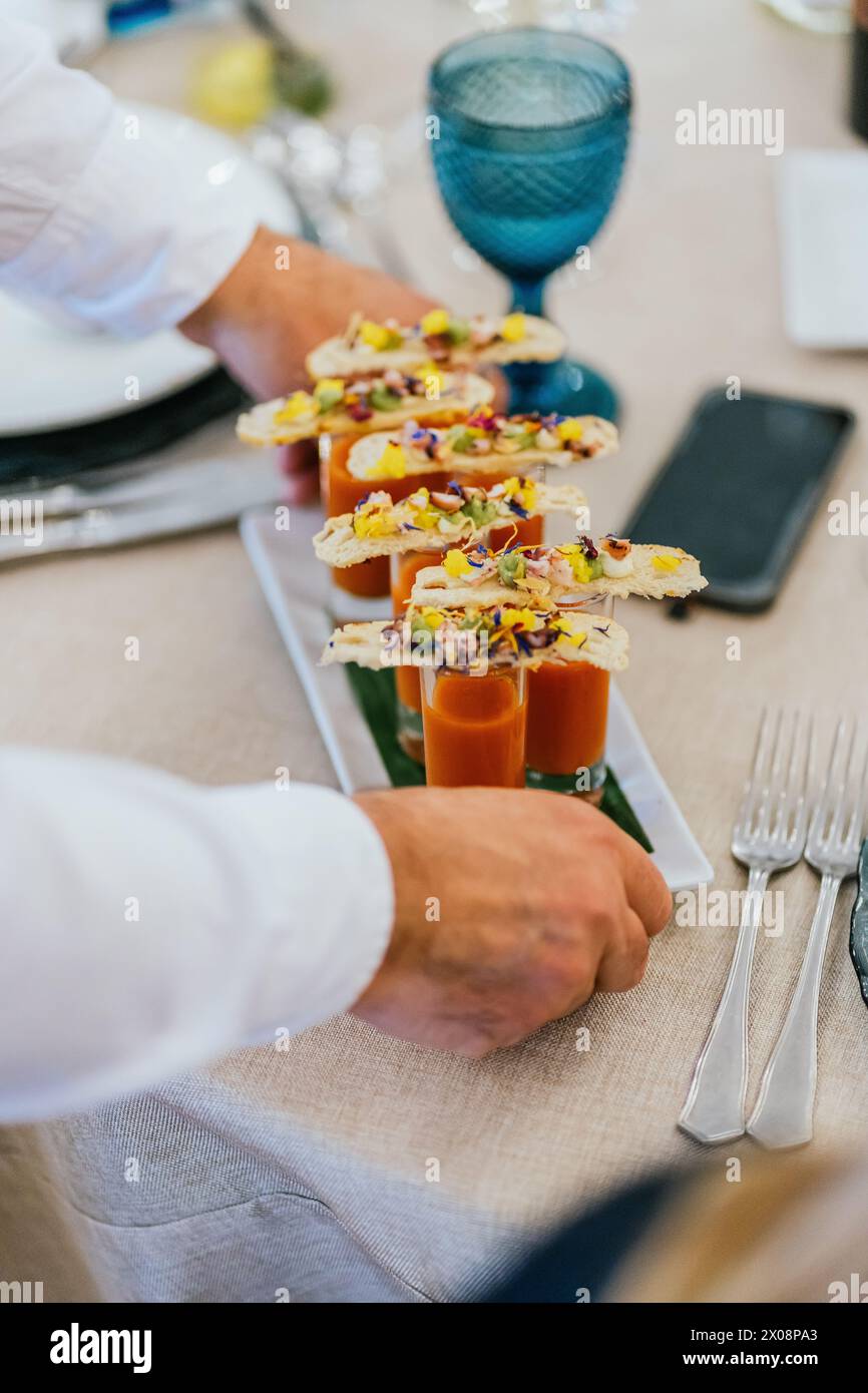 Anonymous chef places gourmet soup shooters with cracker toppings on an ...