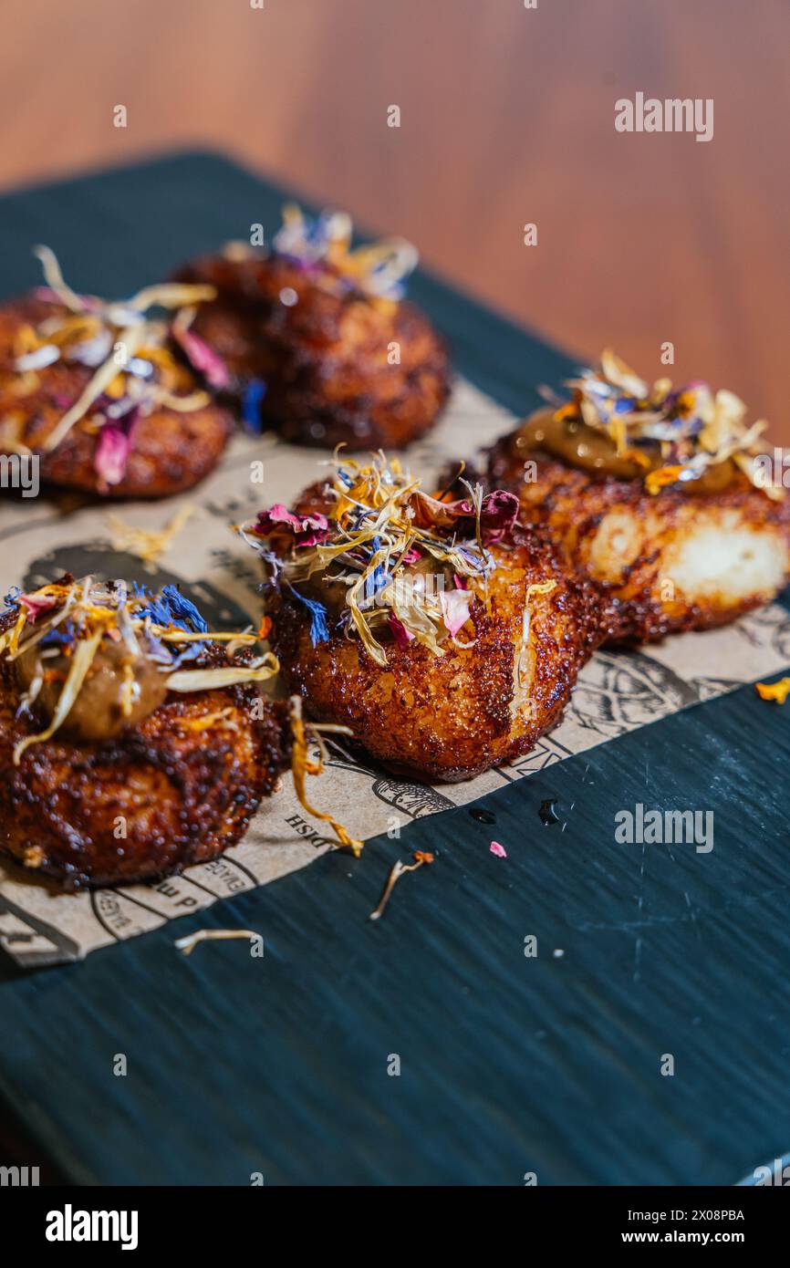 Exquisite crispy patties are garnished with edible flowers and sauce, presented on a slate board for a refined culinary display Stock Photo