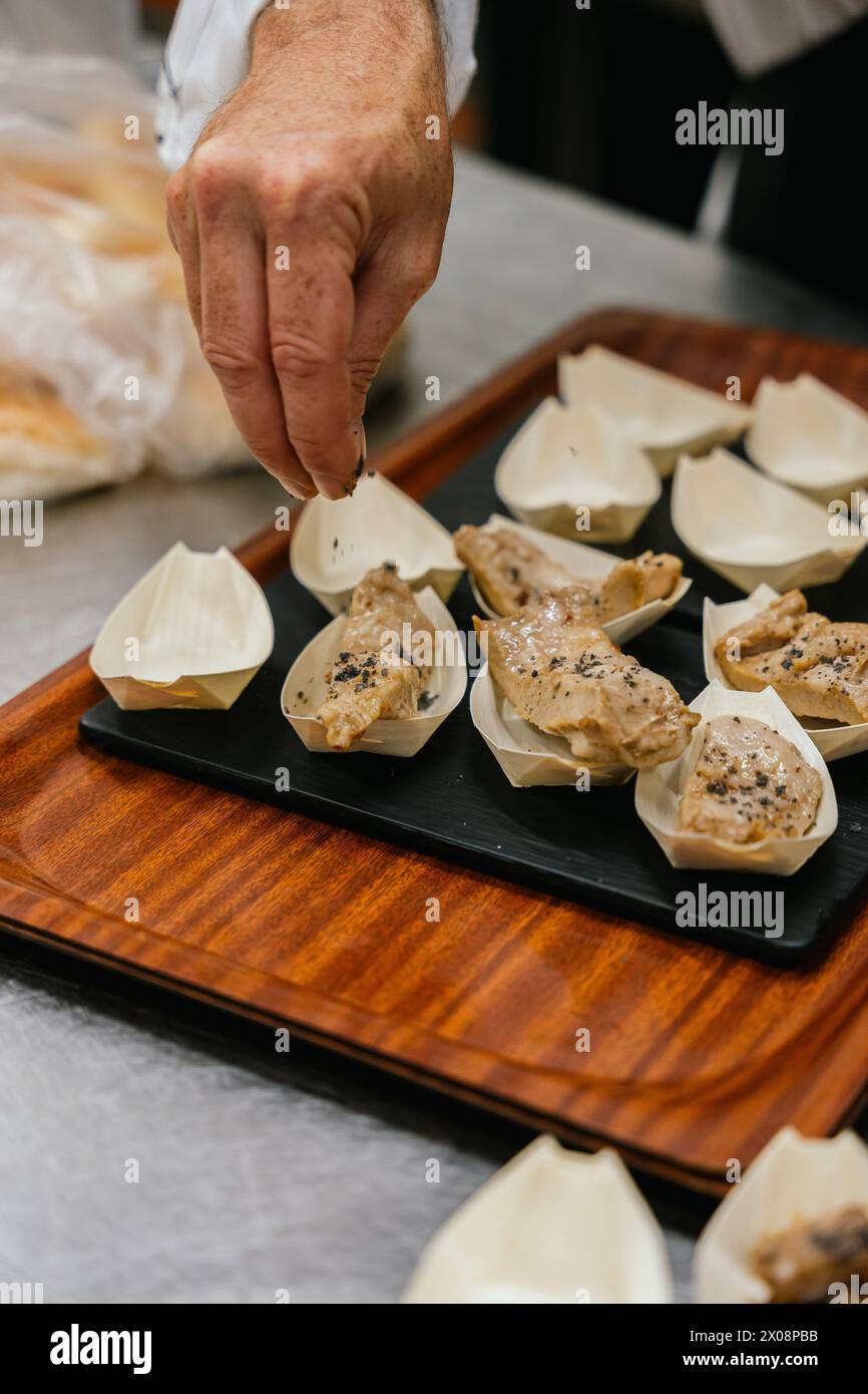 Anonymous chef sprinkles spices over gourmet dumplings delicately placed in individual serving boats on a wooden tray Stock Photo