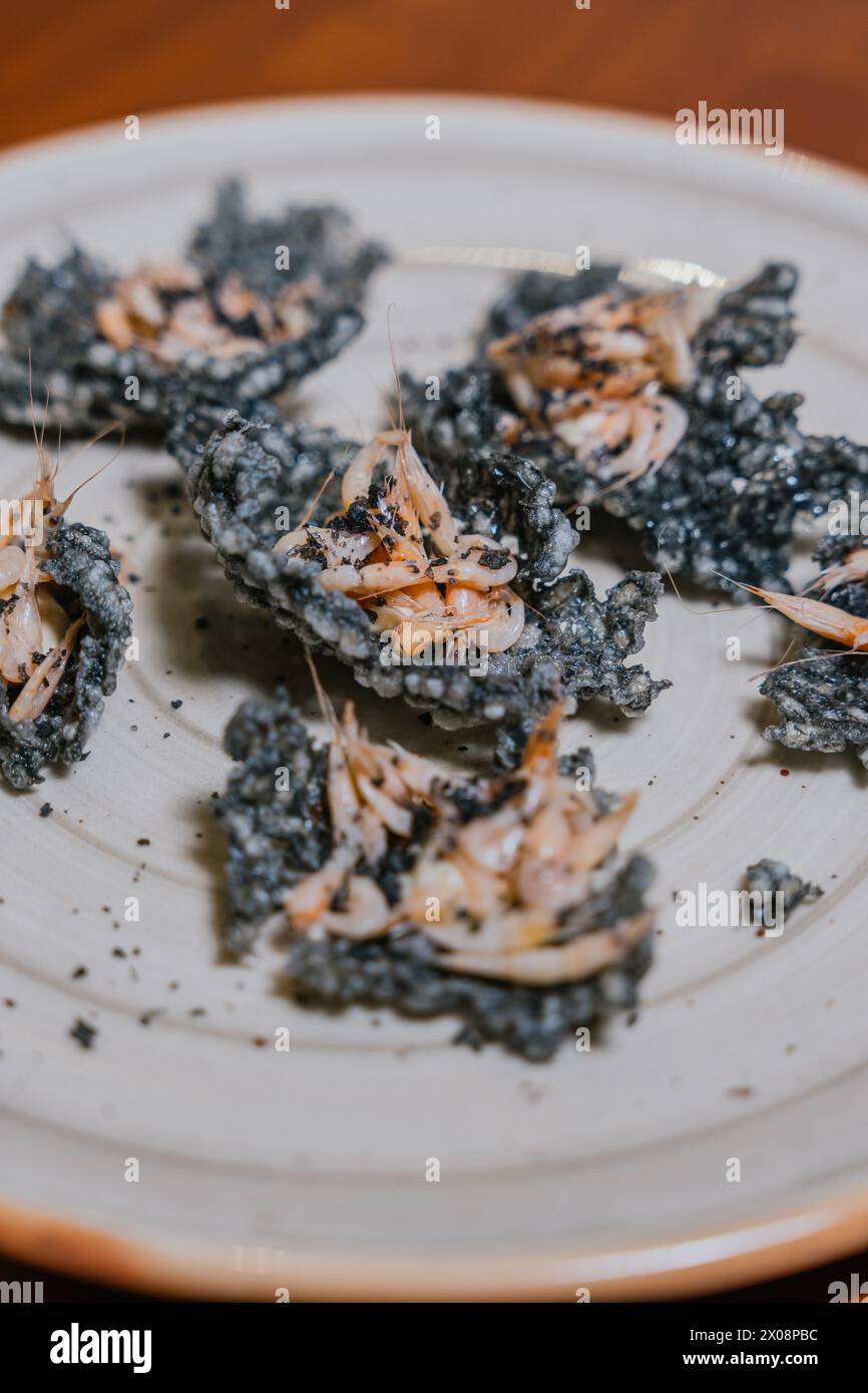 Exquisite charcoal tempura shrimp garnished with delicate herbs on a ceramic plate, embodying sophisticated gastronomy Stock Photo