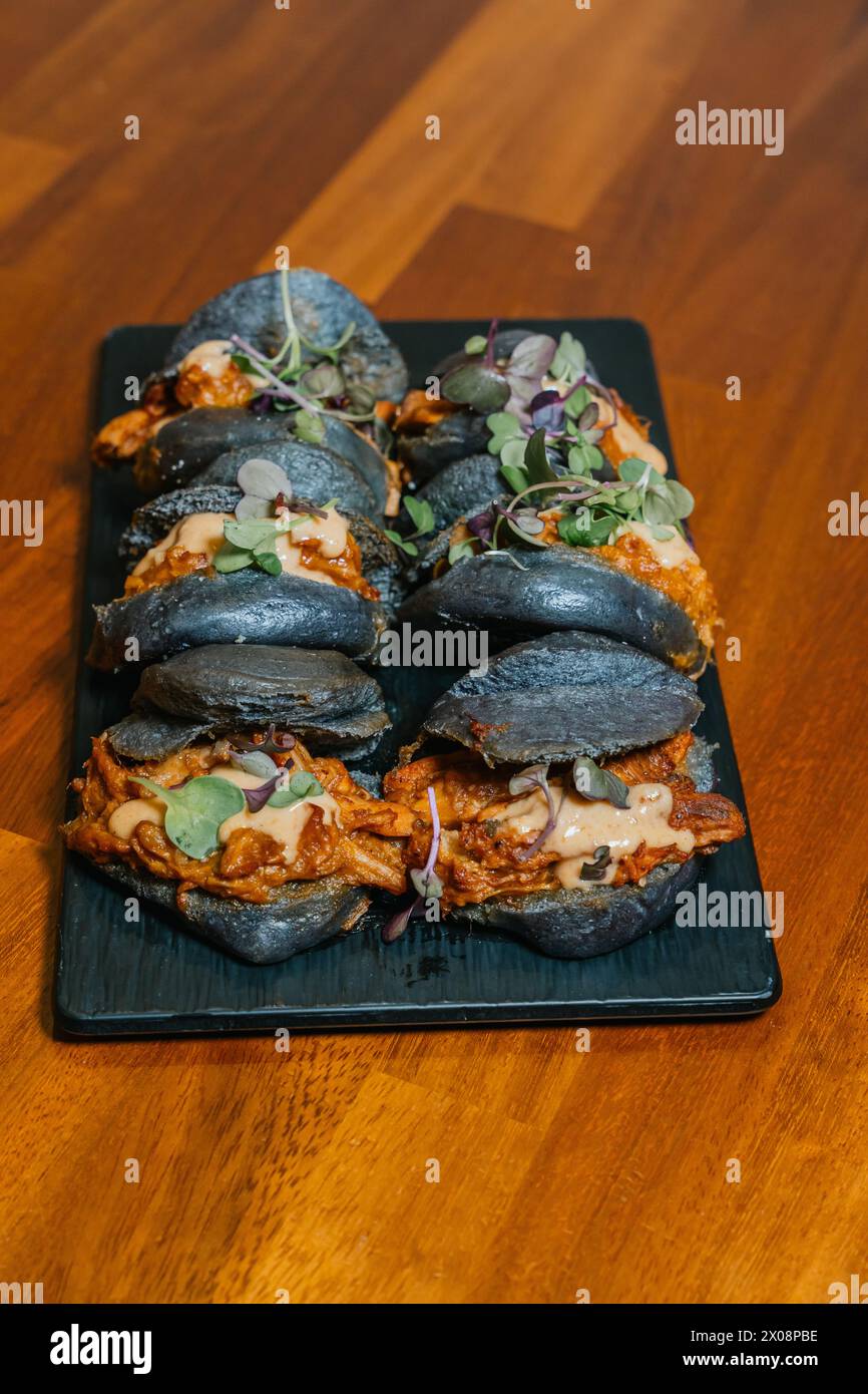 Gourmet sliders with succulent fillings and charcoal buns, adorned with fresh microgreens on a sleek black serving platter Stock Photo