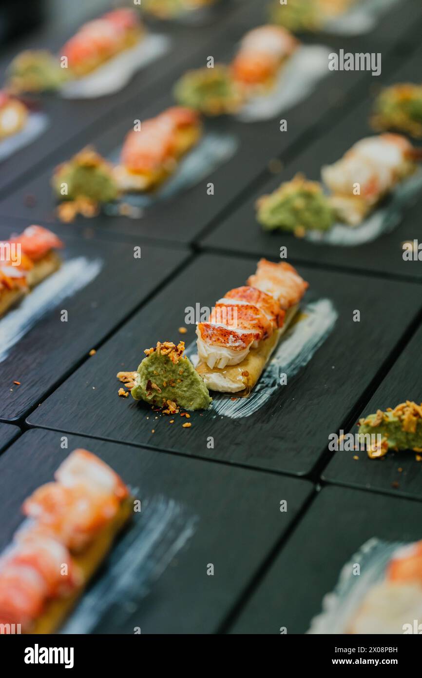 Luxurious lobster canapes paired with a dollop of green sauce, meticulously placed on a chic black slate board for a catered event Stock Photo