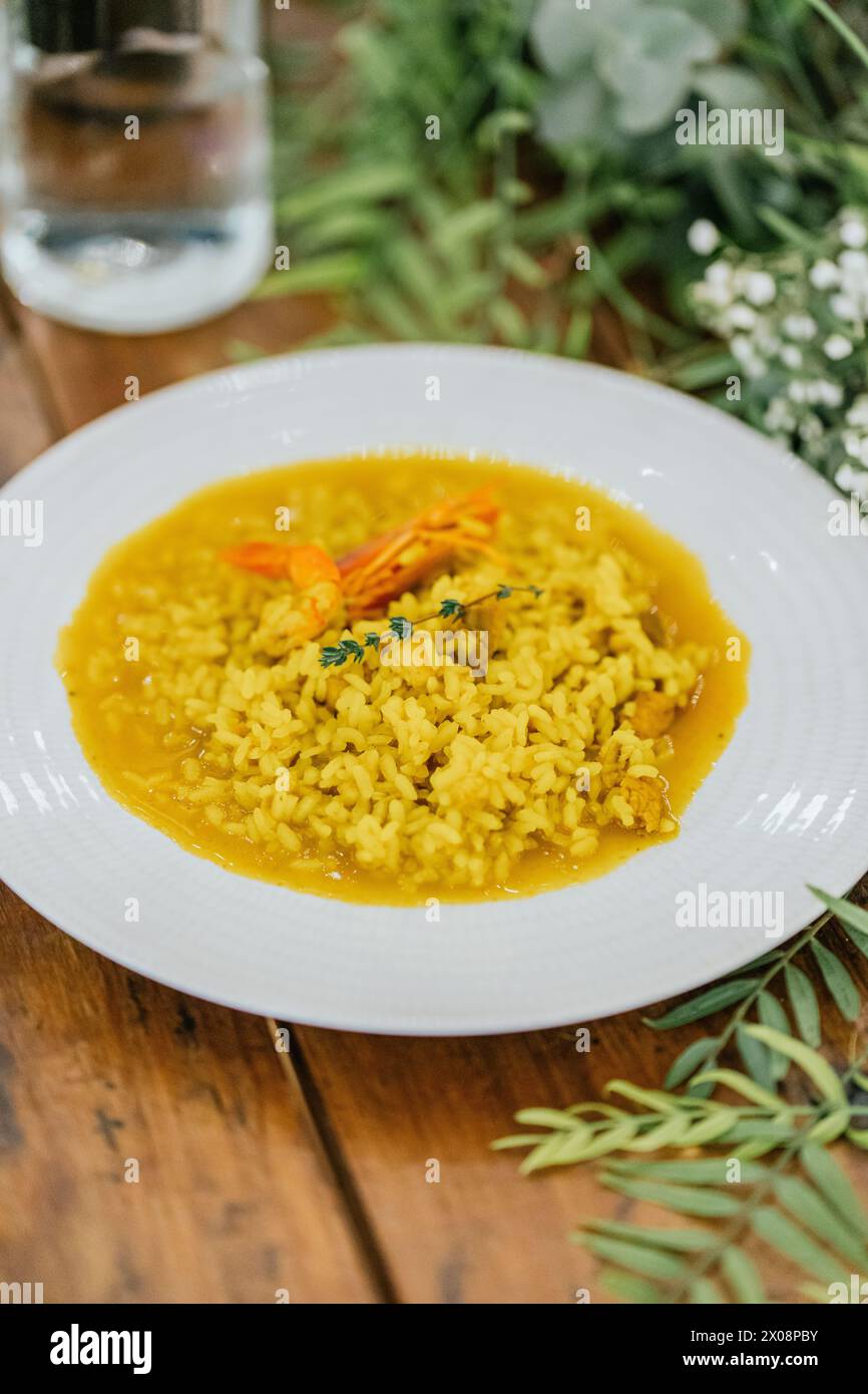 A vibrant plate of shrimp risotto, rich in color and flavor, sits invitingly on a rustic wooden table with a natural, floral backdrop Stock Photo