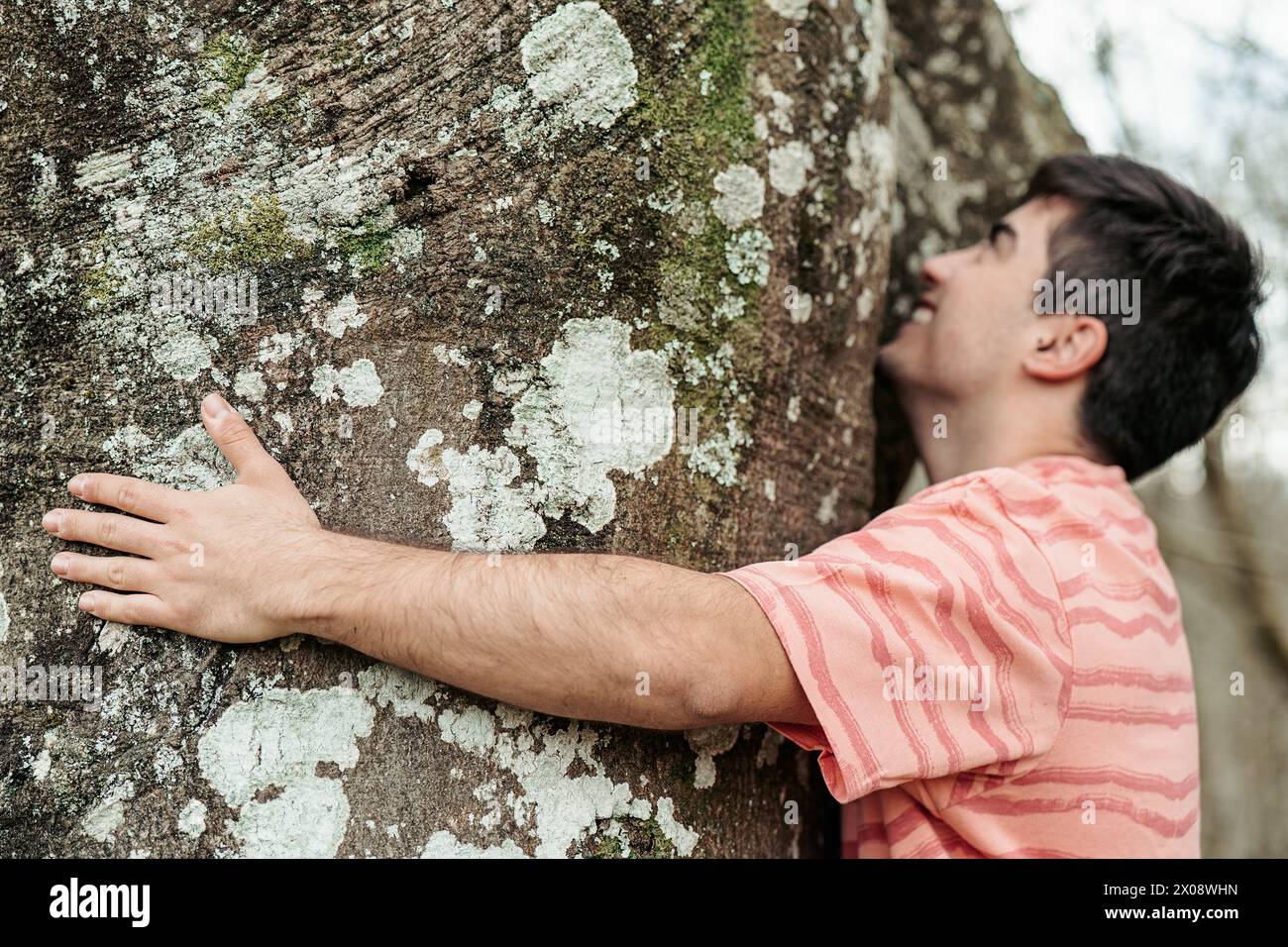 A close-up of a man in contemplative embrace with a large, moss-covered ...