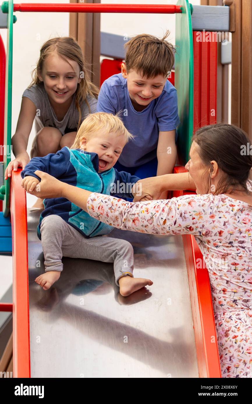 A vibrant and heartwarming scene as a family enjoys time together on a playground slide. The caring mother helps the delighted baby—displaying feature Stock Photo