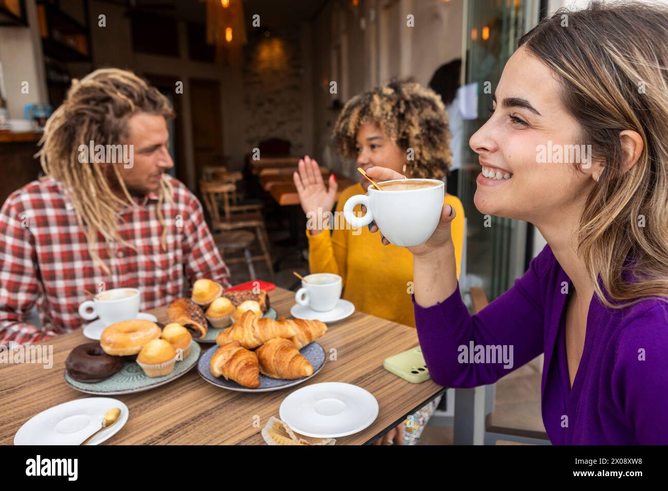 A group of friends is laughing and sharing a good time at a cafe, enjoying a selection of coffee and pastries Stock Photo