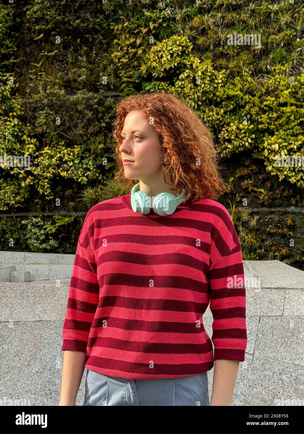 Young redhead woman with curly red hair wearing headphones outdoors Stock Photo