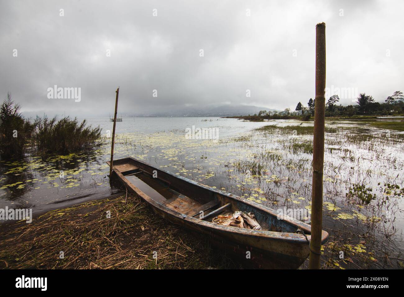 An old wooden boat rests by the reeds on a tranquil, mist-covered lake ...