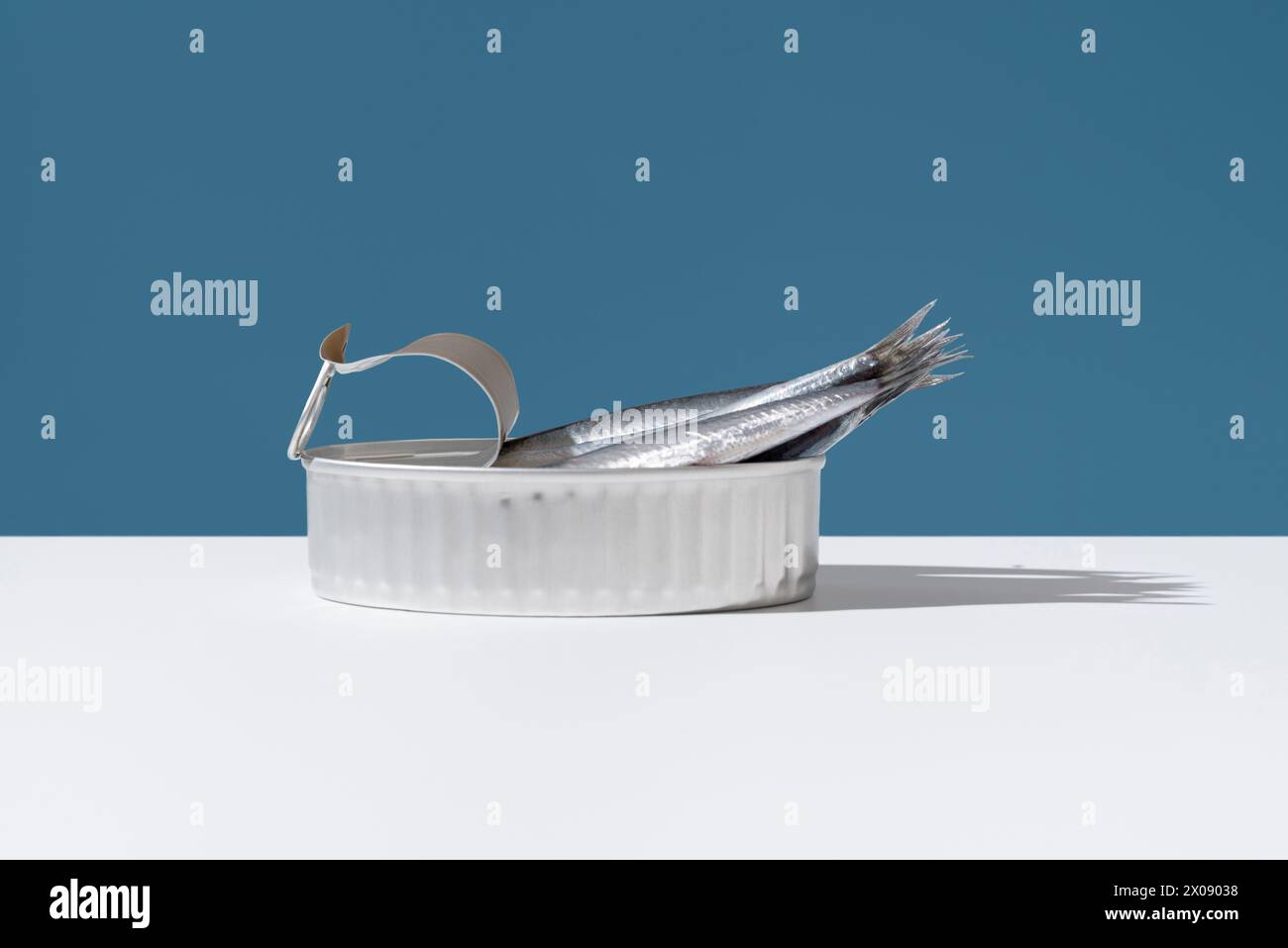 Fresh anchovies extend from an open can, set against a crisp blue background, illustrating a blend of natural and industrial themes Stock Photo