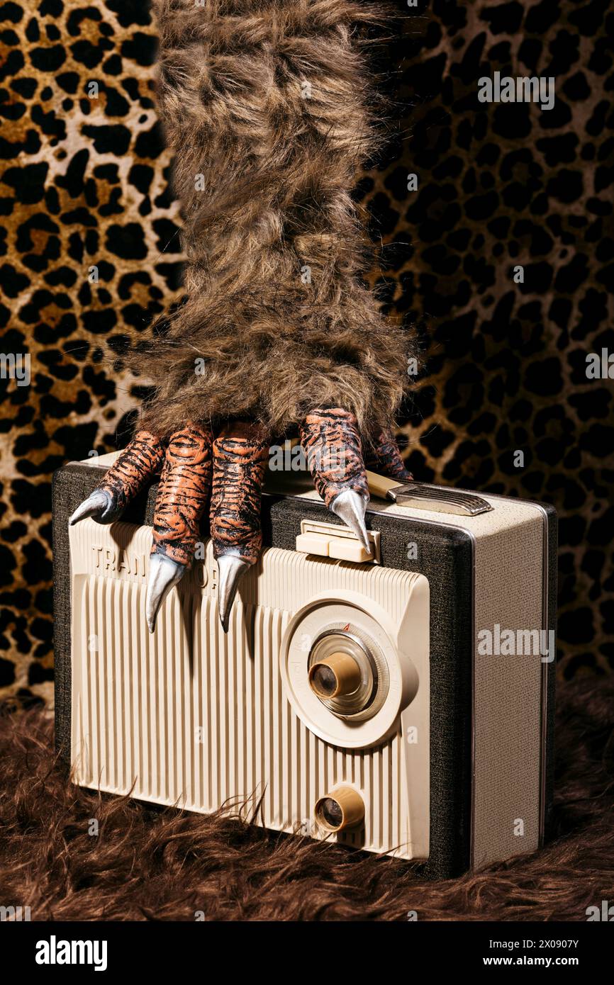 An unusual and creative portrayal with beast-like claws gripping a vintage transistor radio against a leopard print backdrop Stock Photo