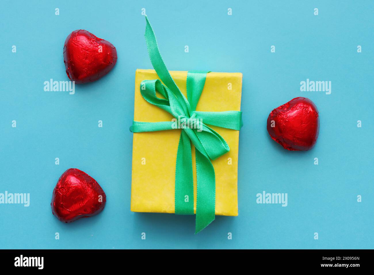 Christmas holiday concept with yellow gift box tied blue ribbon and red heart-shaped candies on a blue paper background... Stock Photo
