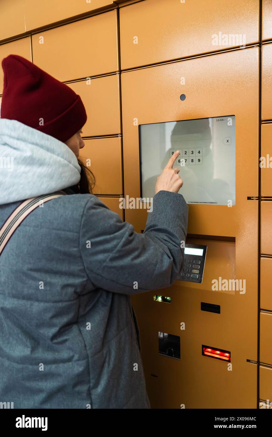 A young woman is entering a security code on a keypad to access an underground parking lot in the city center. The area is dimly lit, and the woman ap Stock Photo