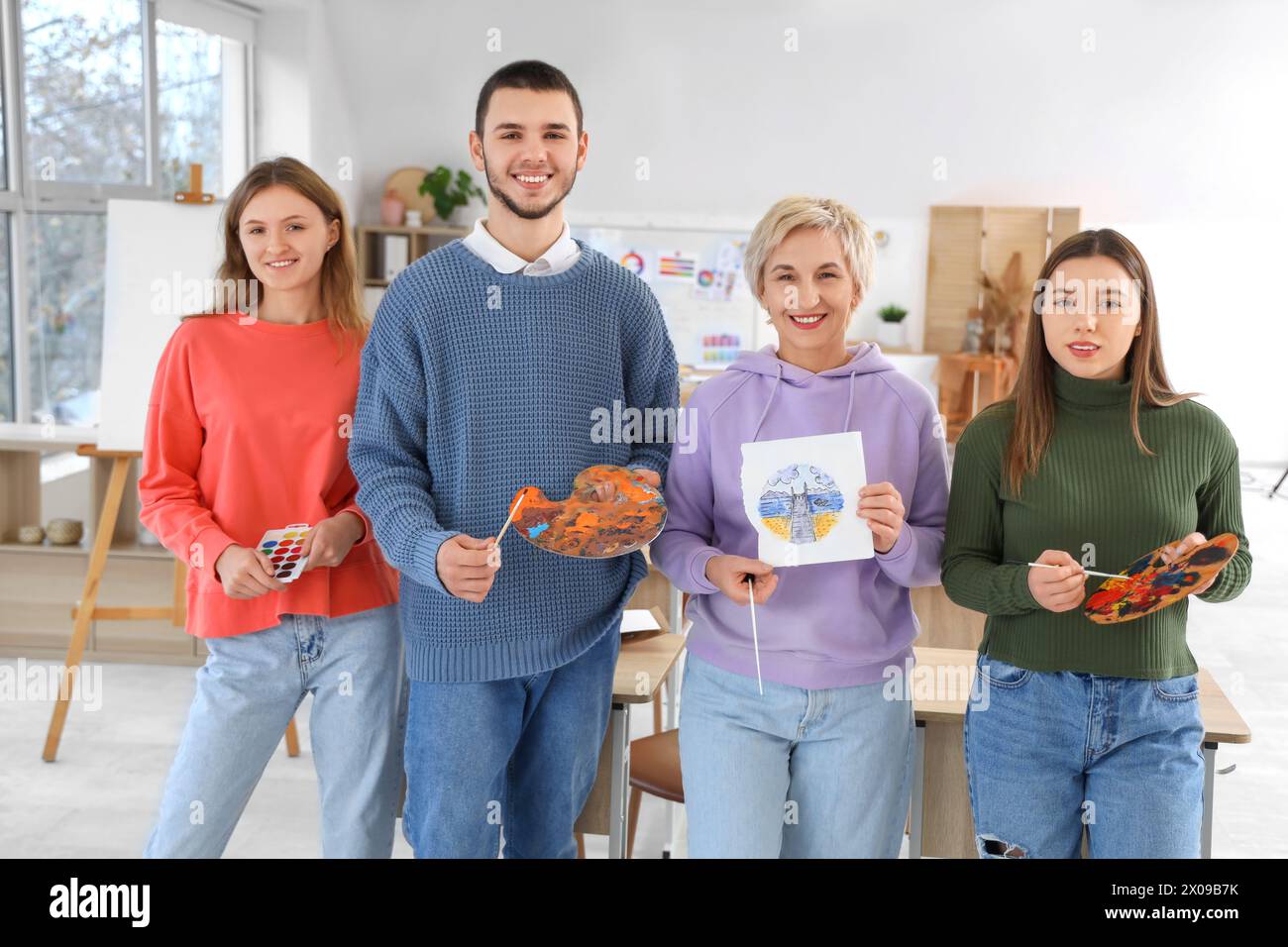 Mature art teacher and students with paints at school Stock Photo