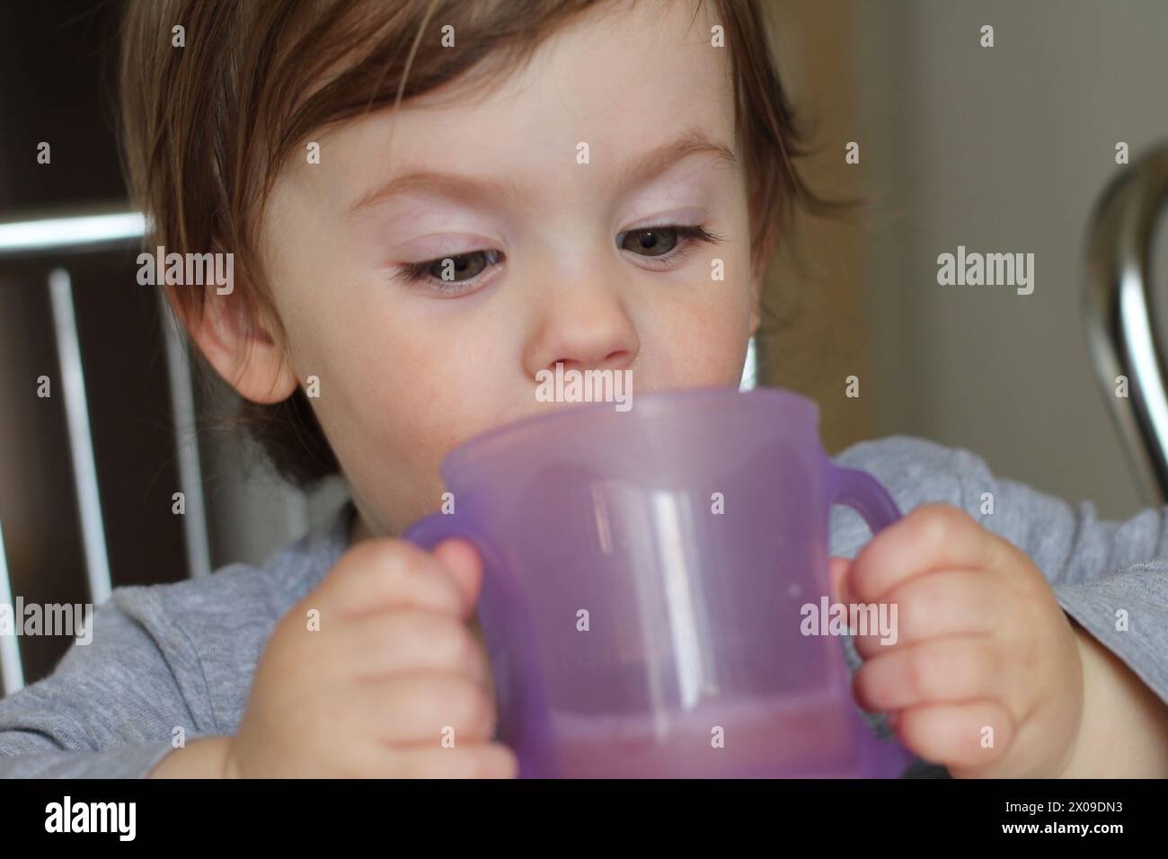 A small child drinks from a two-handed cup. Learning to drink from a cup independently. Developmental milestones and the joy of everyday family life Stock Photo
