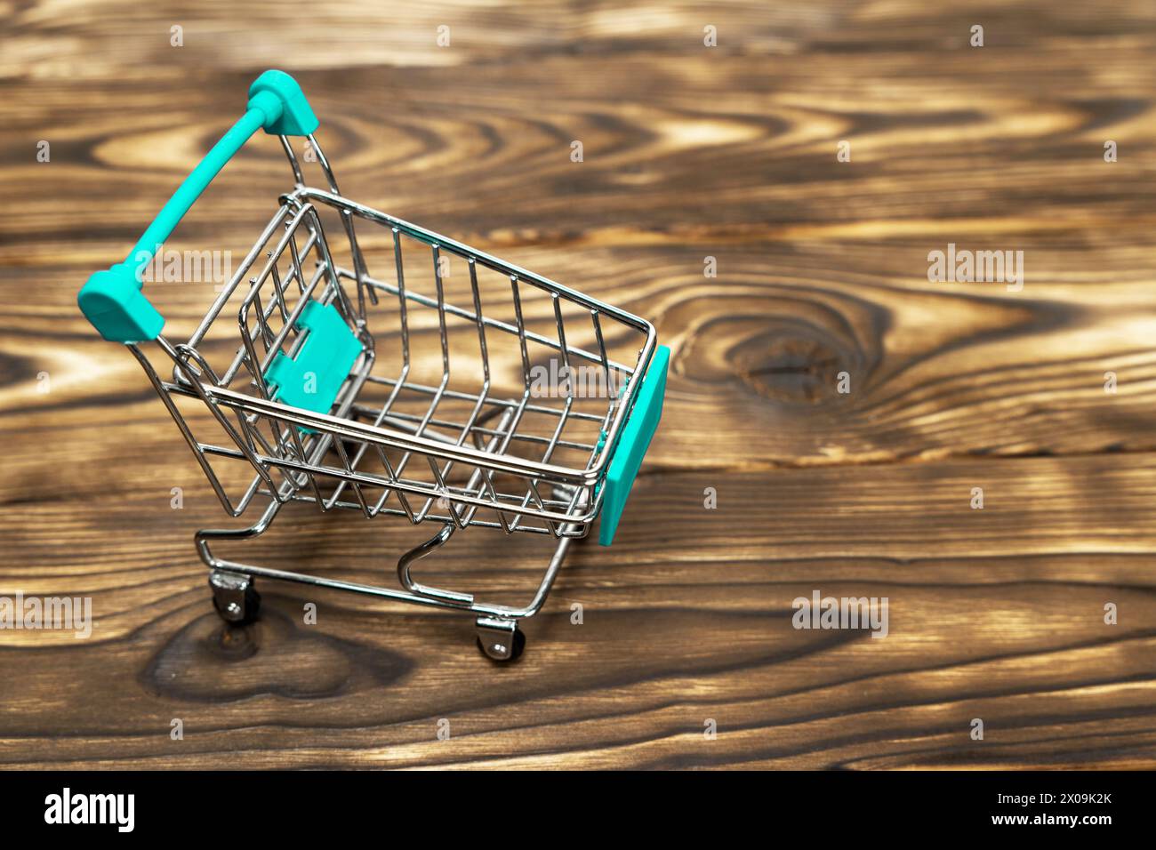 miniature shopping cart on a wooden background. The concept of consumption, holiday purchases, spending. Stock Photo