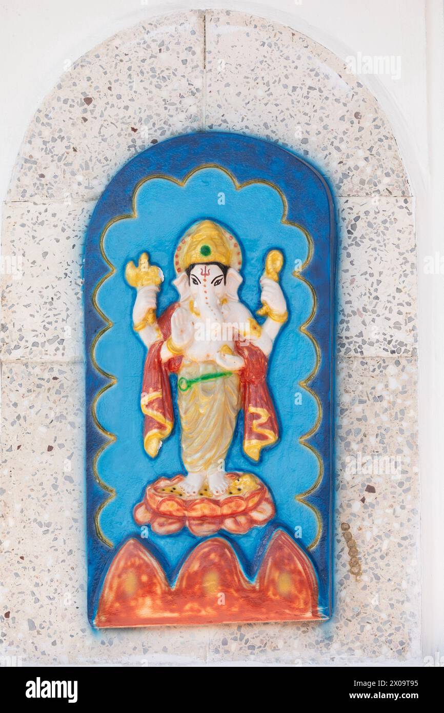 Murti of the Hindu deity Ganesha, standing on a lotus flower and holding a noose, an axe and a sweetmeat, on an exterior wall of the Temple in the Sea Stock Photo
