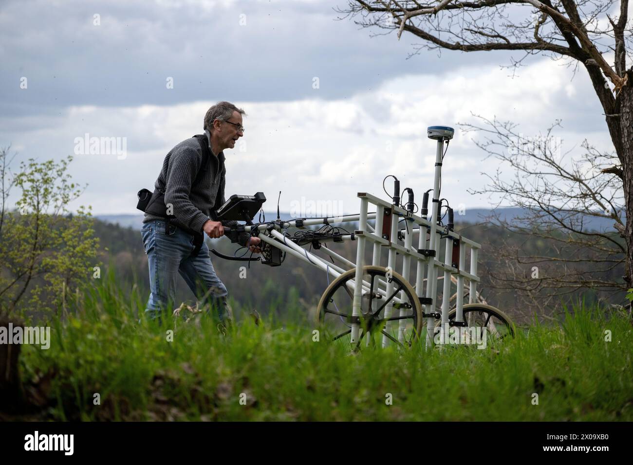 Altenstein, Germany. 10th Apr, 2024. Graduate geologist Markus Tarasconi pushes a geomagnetic investigation device on a vantage point near Altenstein. By using highly sensitive magnetometers, anomalies in the ground can be measured and their distribution displayed on maps without having to dig into the ground. A place of execution and a gallows are thought to have been located below the ruins of Altenstein Castle. Credit: Pia Bayer/dpa/Alamy Live News Stock Photo