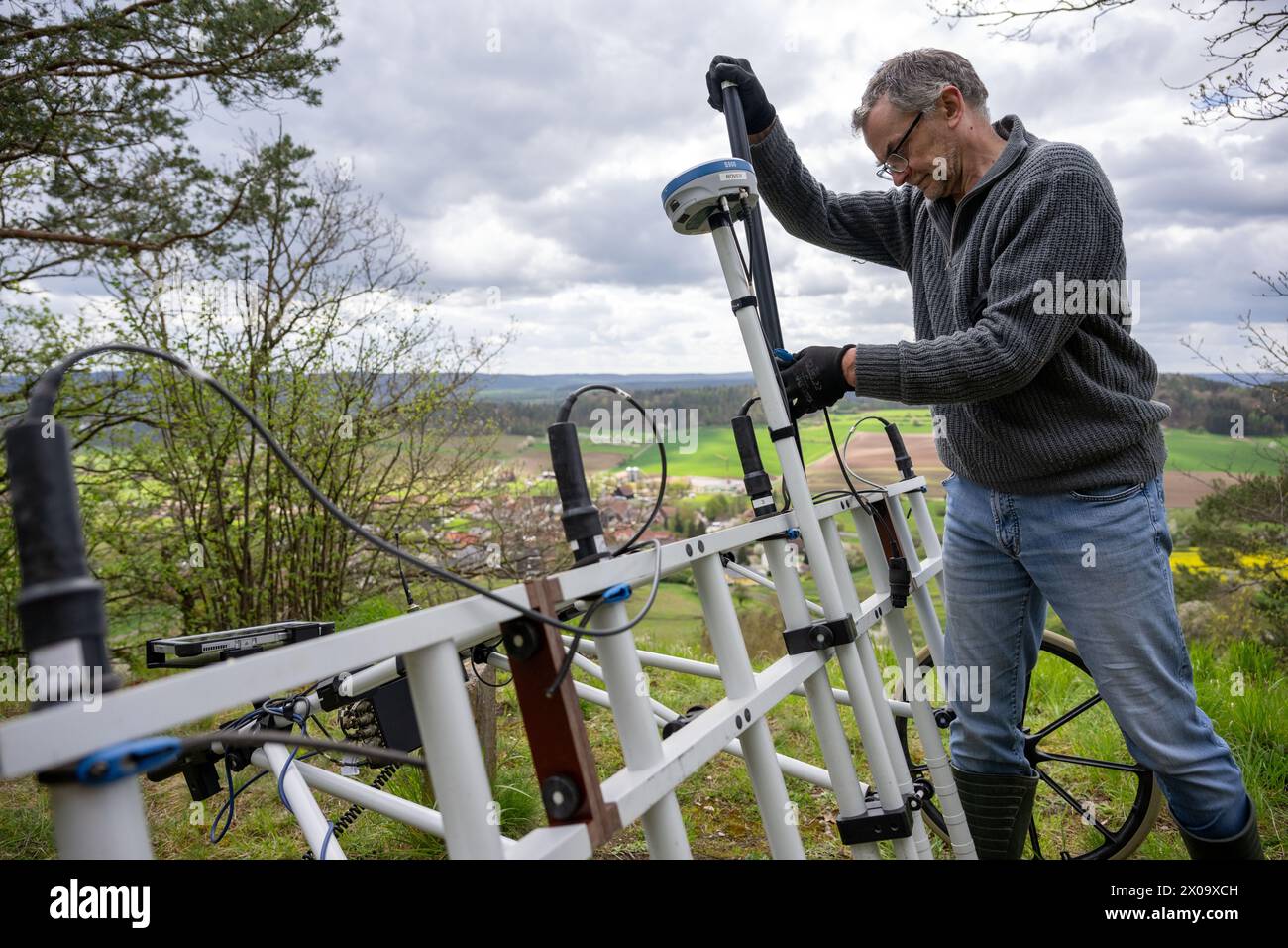 Altenstein, Germany. 10th Apr, 2024. Graduate geologist Markus Tarasconi prepares a geomagnetic investigation device for a new series of measurements at a vantage point near Altenstein. By using highly sensitive magnetometers, anomalies in the ground can be measured and their distribution displayed on maps without having to dig into the ground. A place of execution and a gallows are thought to have been located below the ruins of Altenstein Castle. Credit: Pia Bayer/dpa/Alamy Live News Stock Photo