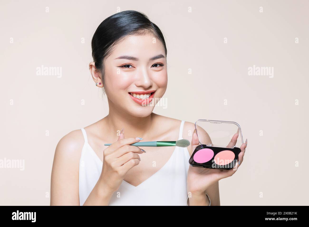 Young asian smiling woman holding blush palette with a brush isolated on a beige background Stock Photo