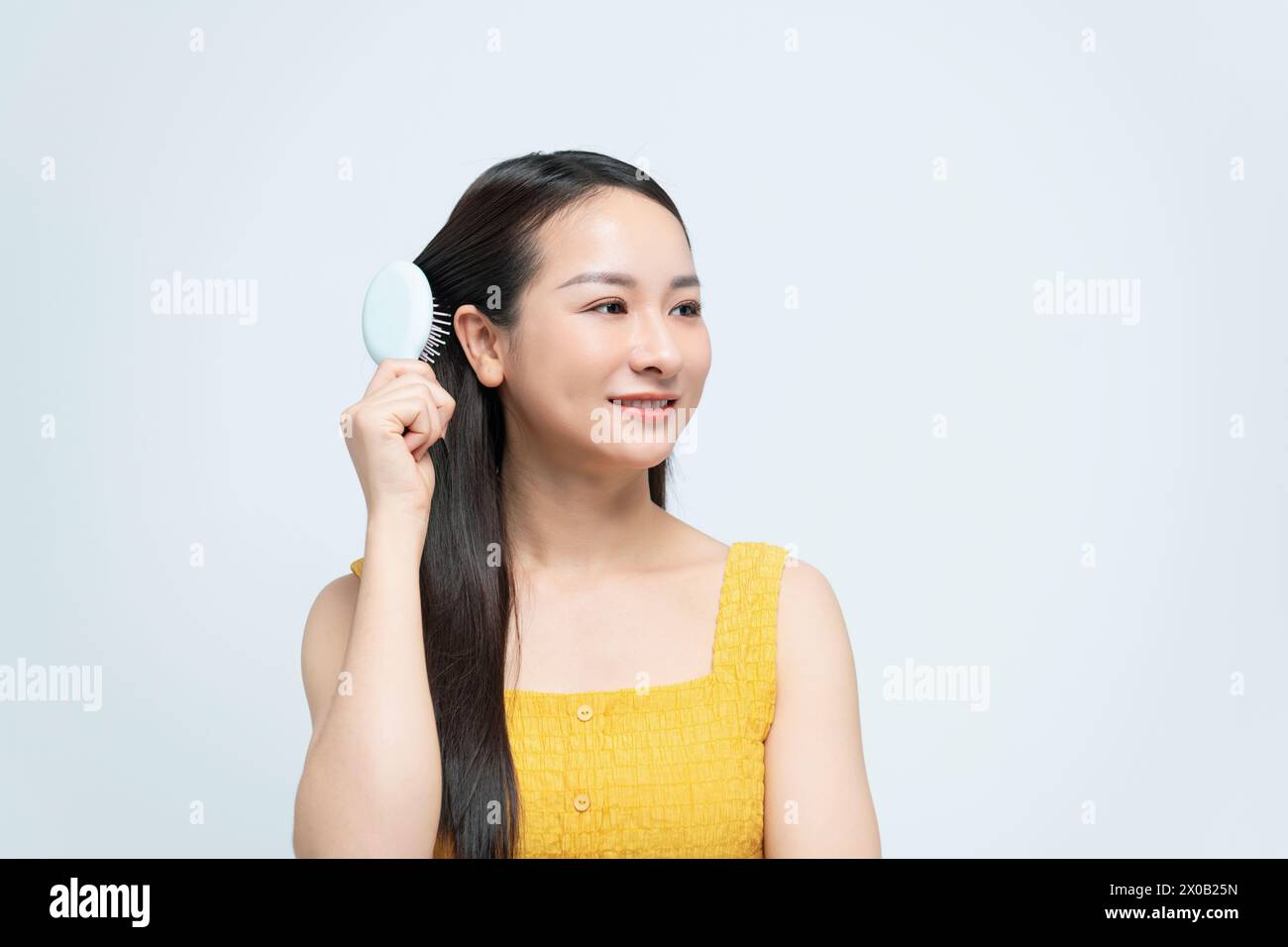 Happy young woman combing her long healthy hair on white background. Stock Photo