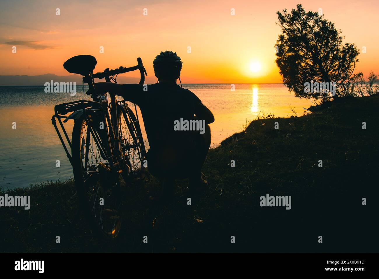 Silhouette of cyclist traveler with his bicycle enjoy sunset view together by tranquil Sevan lake in nature. Bicycle touring outdoors in nature Stock Photo