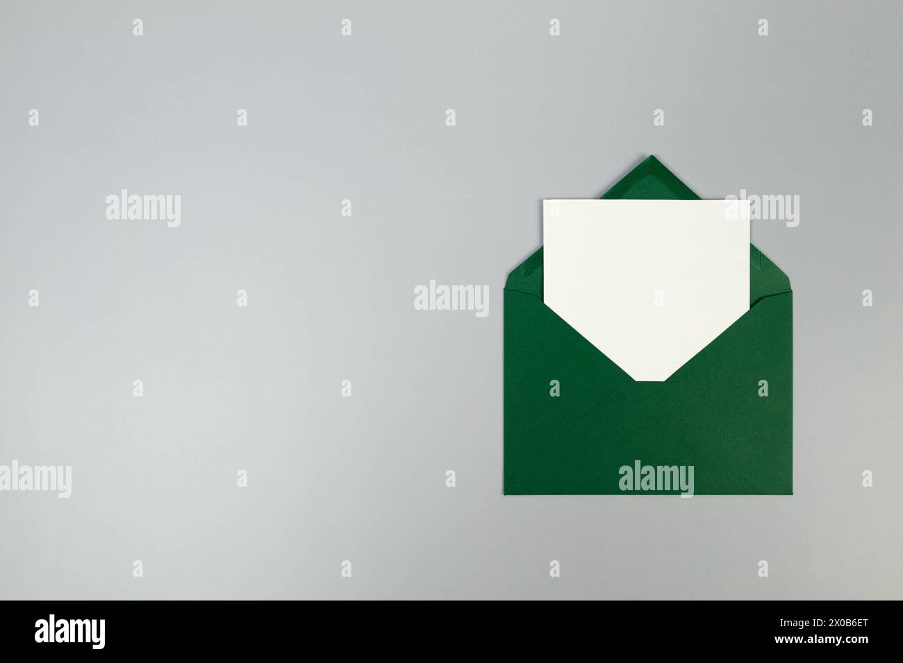 Top view of green envelope, white card on grey background. Post flat lay. Copy space. Stock Photo