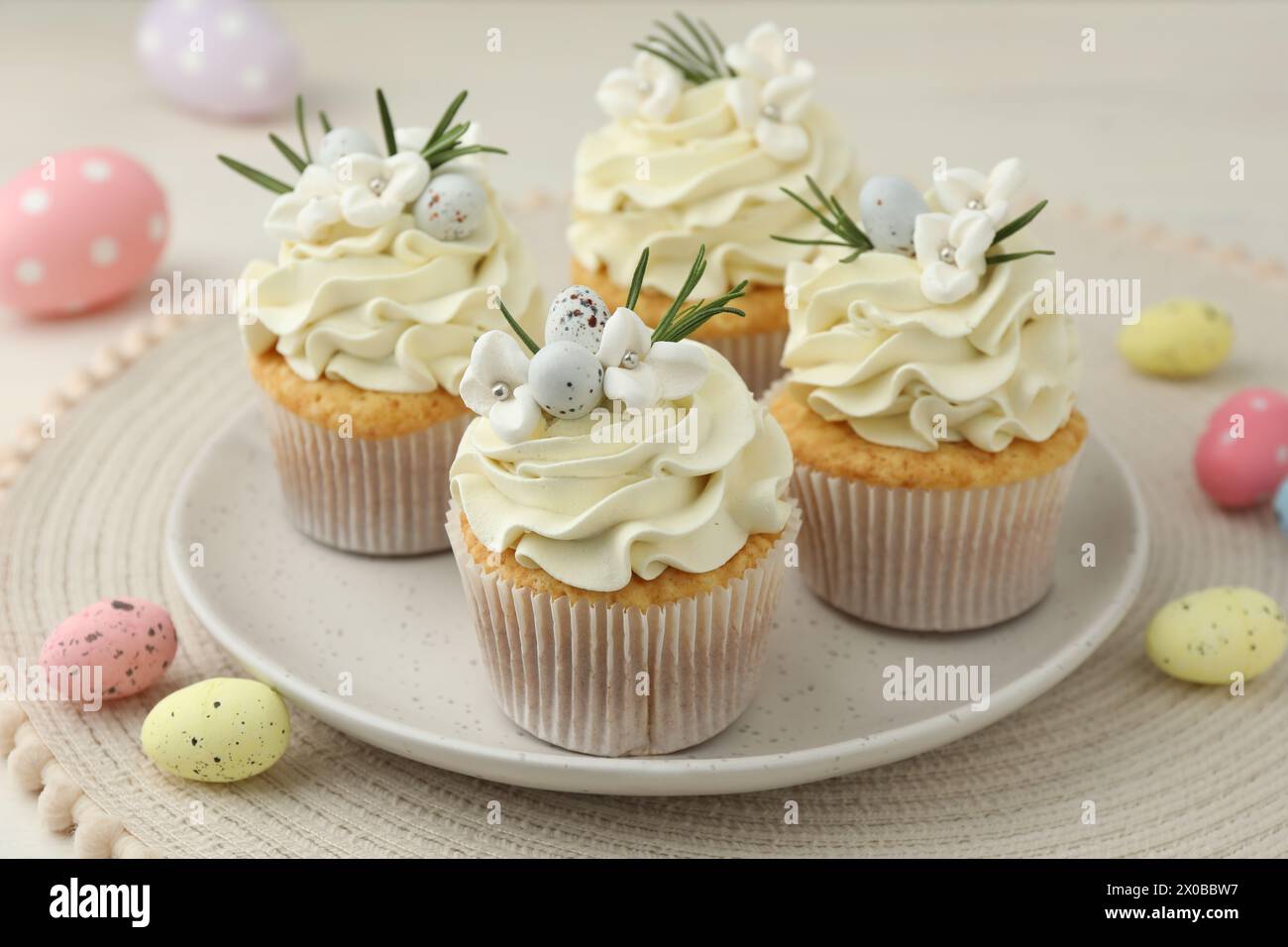 Tasty Easter cupcakes with vanilla cream and candies on table Stock Photo