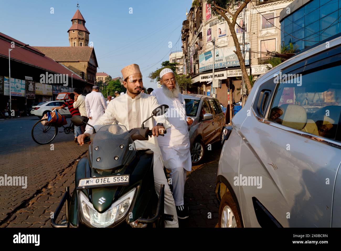 On the occasion of Eid (Id) Festival, a Muslim man takes an outing on his scooter in Mumbai, India; b/g left: Crawford Market with its iconic tower Stock Photo