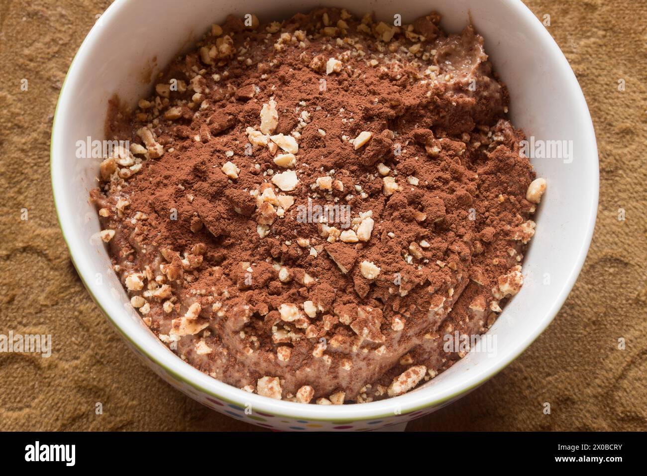 Overhead view of a bowl of creamy, homemade chocolate dessert, sprinkled with crushed almonds and nuts, and dusted with cocoa powder on a velvet chair Stock Photo