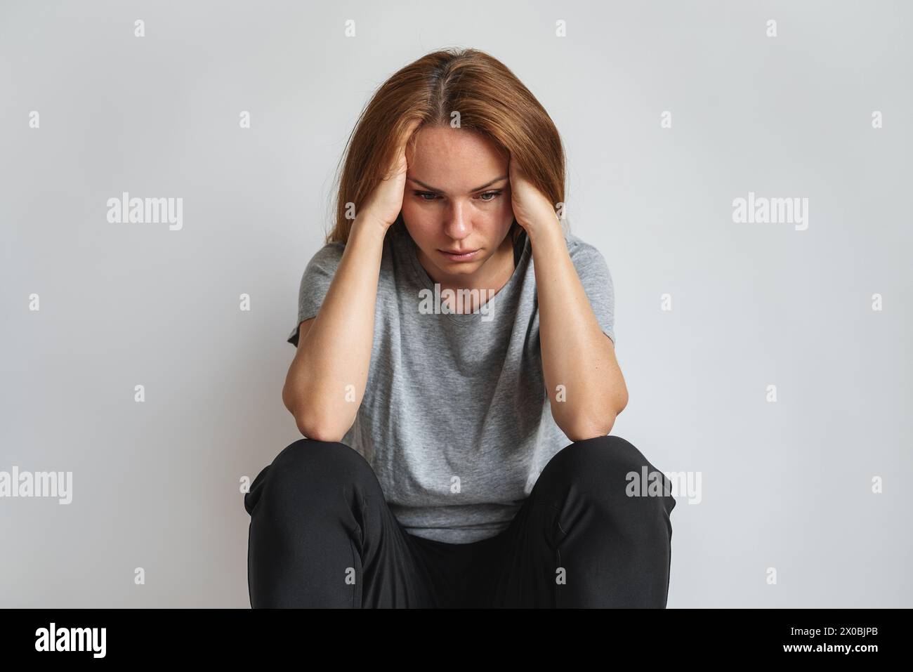 Hopeless concept. PTSD. Alone depressed woman sits next to wall and holds head with her hands. Stock Photo