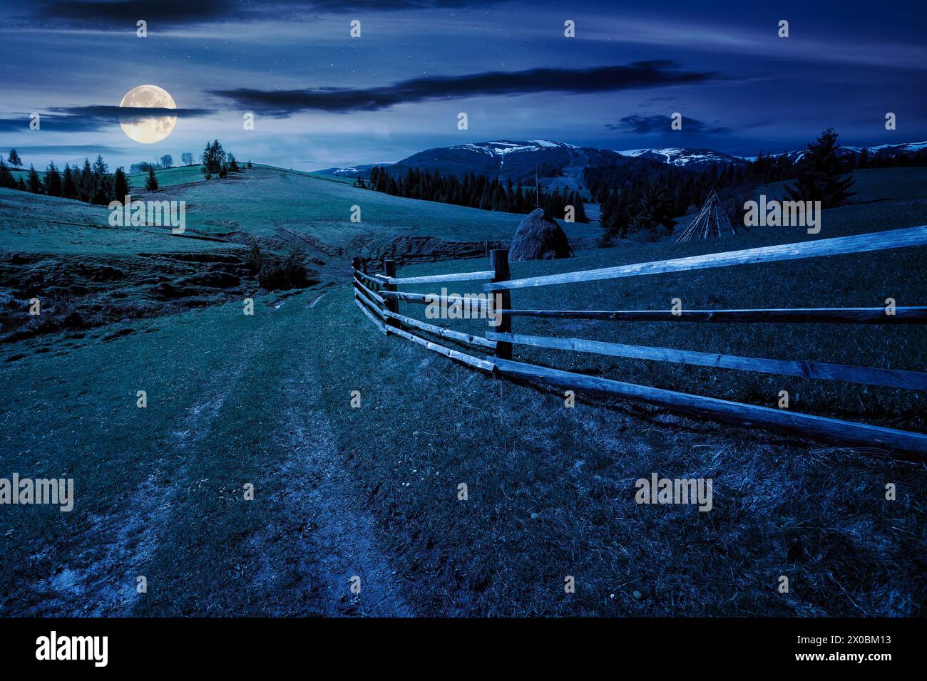 carpathian countryside scenery in spring at night. mountainous rural landscape with path through the meadow and haystack behind the wooden fence in fu Stock Photo
