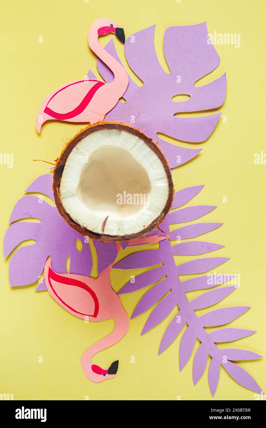 Broken coconut, paper tropical leaves and flamingos on a light yellow background. Summer background, flat lay. Stock Photo