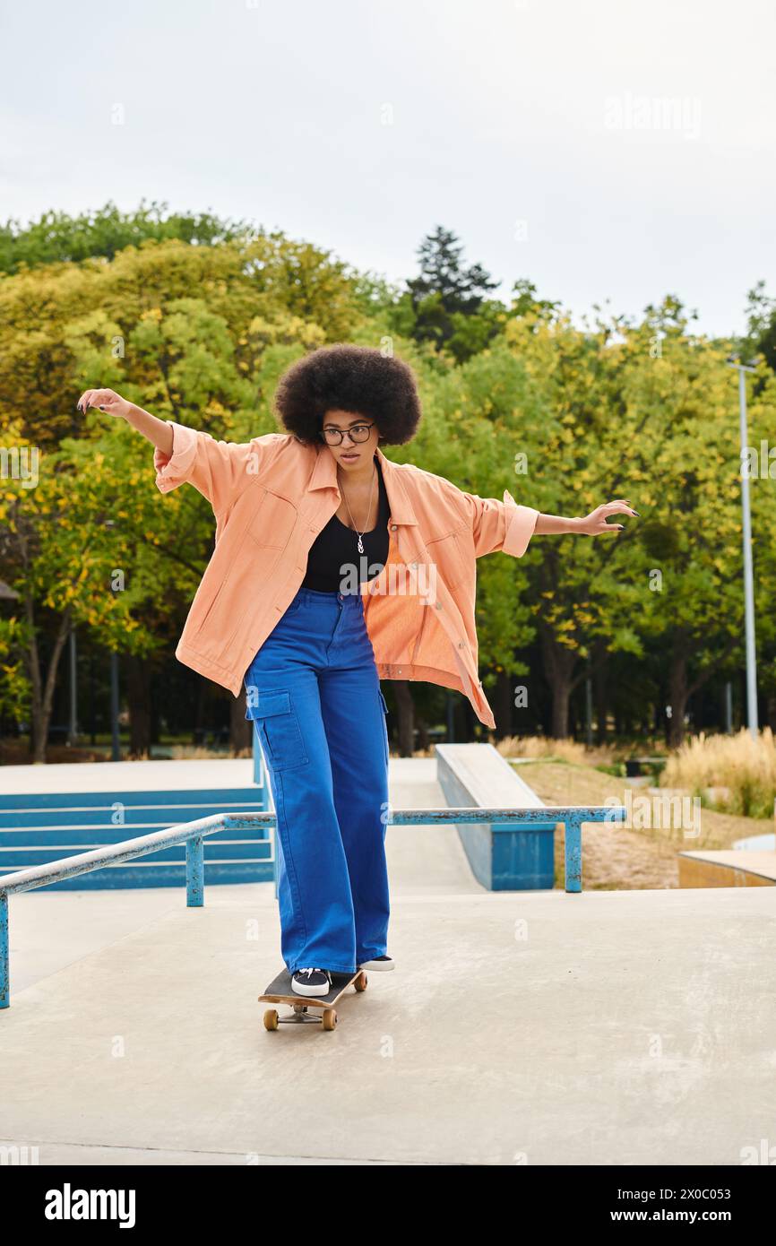 A young African American woman with curly hair effortlessly rides a skateboard on top of a cement slab in an urban skate park. Stock Photo