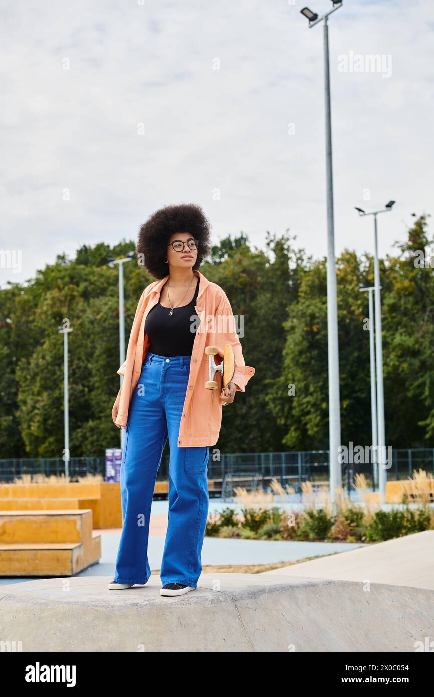 A young Afro-American woman with curly hair confidently stands atop a skateboard ramp in a skate park, ready for her next move. Stock Photo