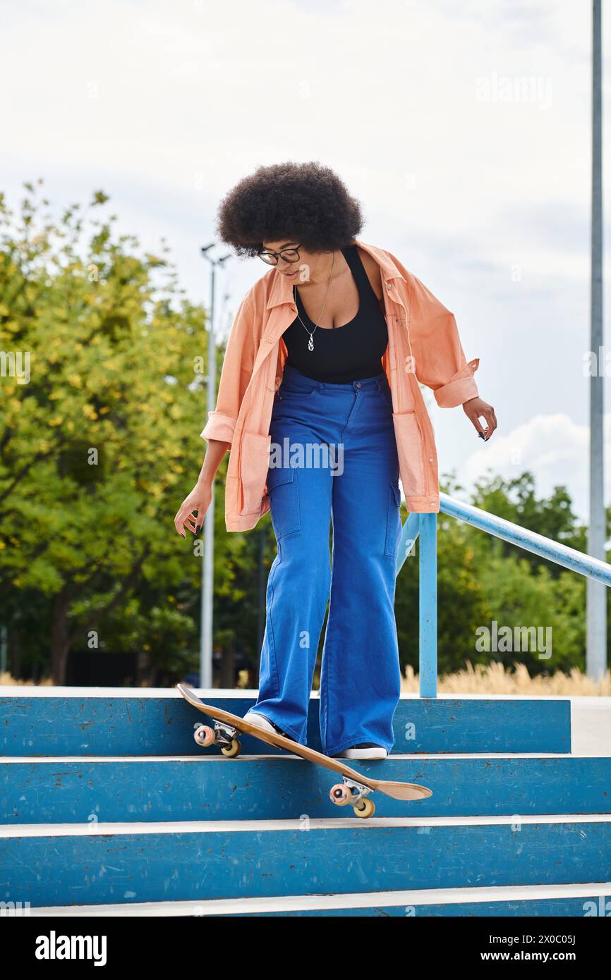 A talented young African American woman with curly hair skillfully rides her skateboard down a flight of stairs at a skate park. Stock Photo