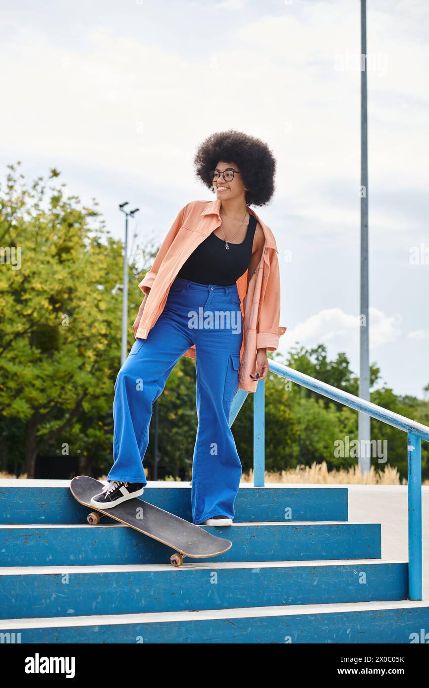 An African American woman with curly hair skillfully skateboarding down a staircase in an urban skate park. Stock Photo