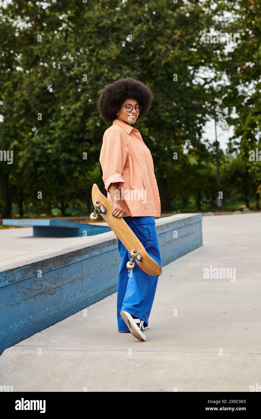 A young man of African descent with curly hair confidently holds a skateboard in a vibrant skate park setting. Stock Photo