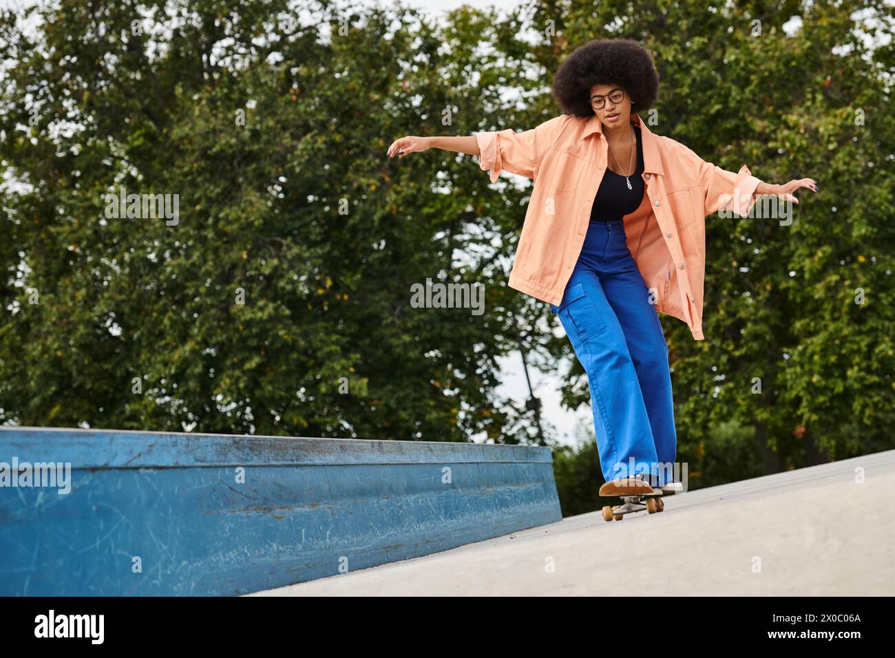 A young African American woman with curly hair skillfully riding a skateboard down the side of a ramp in a vibrant skate park. Stock Photo