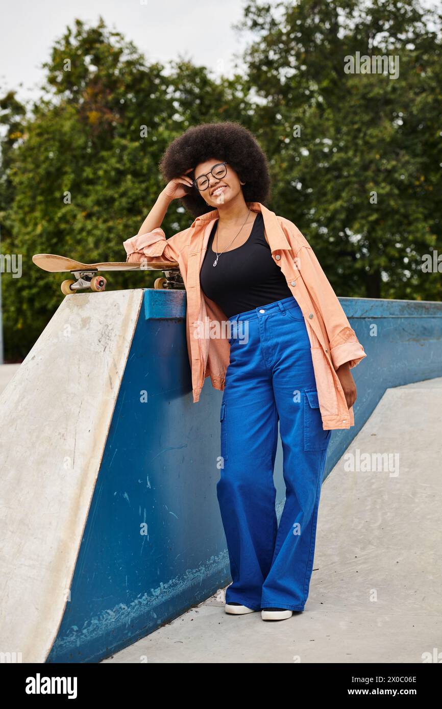 A young African American woman with curly hair skillfully skateboarding next to a ramp in an outdoor skate park. Stock Photo