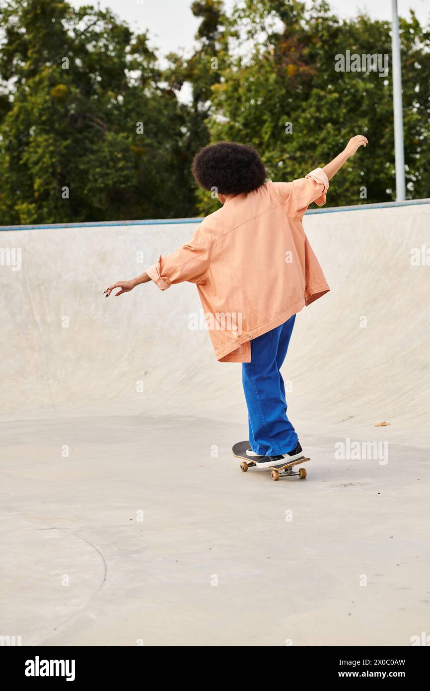A young African American boy with curly hair confidently rides his skateboard at a bustling skate park. Stock Photo